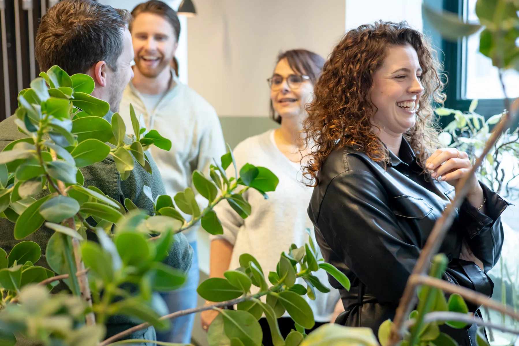 Diverse teamleden bouwen samen aan werkplezier en verbinding rond groene planten op het kantoor.
