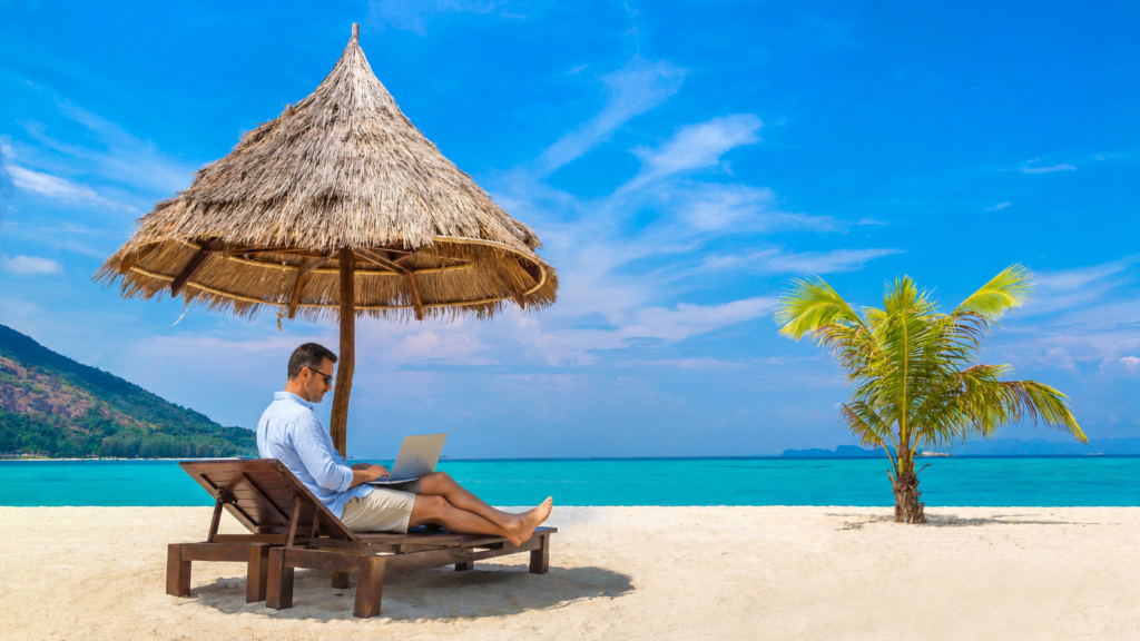 Man werkt op laptop op het strand als beeld van vakantie werkplezier en niet kunnen loslaten.